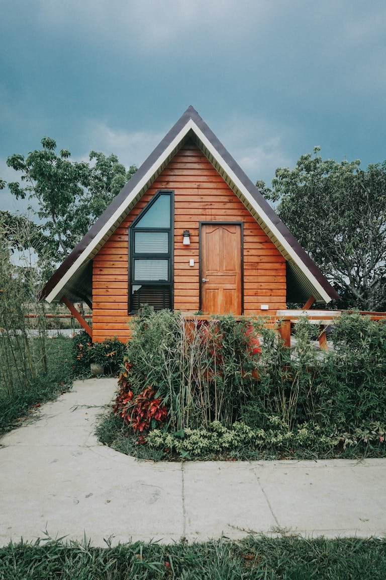 Best tiny home. A charming wooden A-frame cabin surrounded by lush greenery and gardens, perfect for a peaceful retreat.